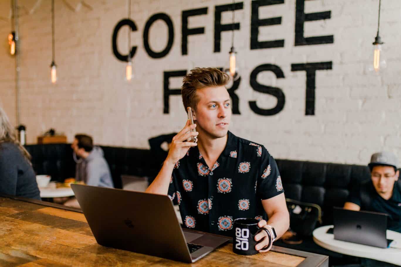 Man On Phone And Using A Computer in A Coffee Bar